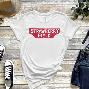 May include: White t-shirt with a red vintage-style sign that says "STRAWBERRY FIELD" printed on the front.