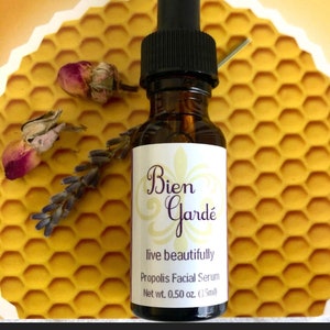 May include: A small amber glass bottle with a black dropper top. The bottle is labeled "Bien Gard&eacute;" with the text "live beautifully" and "Propolis Facial Serum". The bottle contains 0.50 ounces (15 ml) of serum.