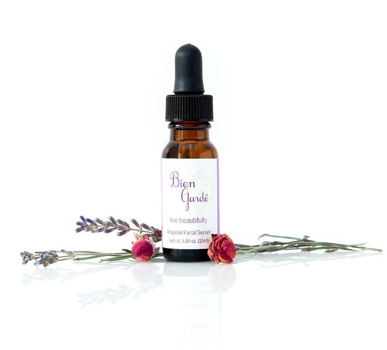 May include: A brown glass bottle with a dropper top, labeled "Bien Gard&eacute;" and "live beautifully  -  Rosehips Facial Serum -  net wt 0.50 oz (15ml)". The bottle is surrounded by dried lavender and rose buds.