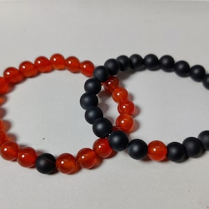 May include: Two bracelets, one with orange carnelian beads and one with black matte beads.
