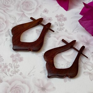 May include: A pair of dark brown wooden earrings with a unique teardrop shape. The earrings are made of wood and have a simple design.