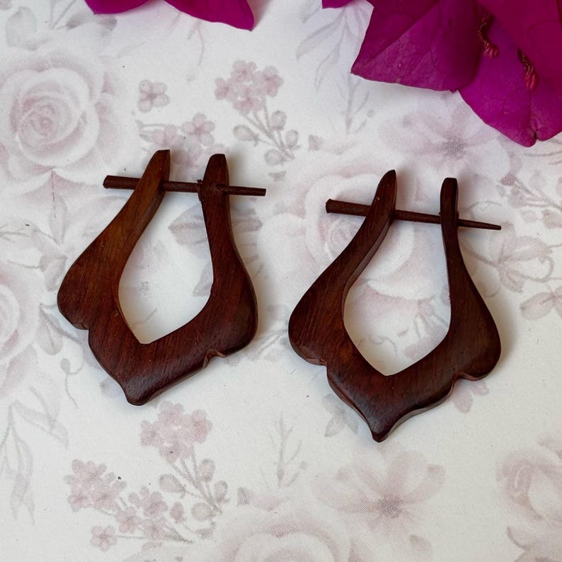 May include: A pair of dark brown wooden earrings with a unique, curved design. The earrings are made of wood and have a natural finish.