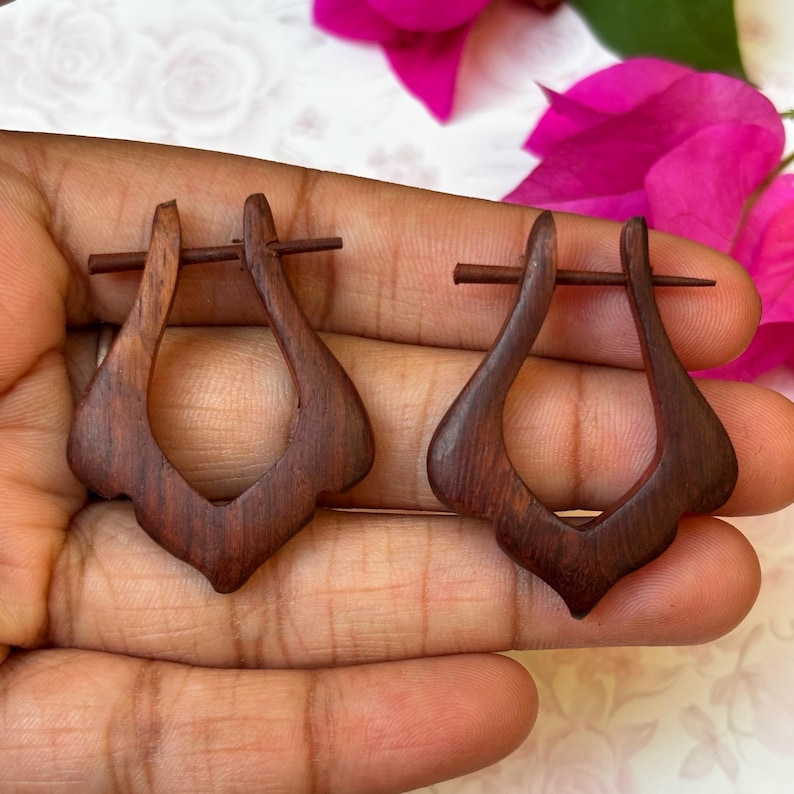May include: A pair of dark brown wooden earrings with a unique teardrop shape. The earrings are held together by a small metal pin.