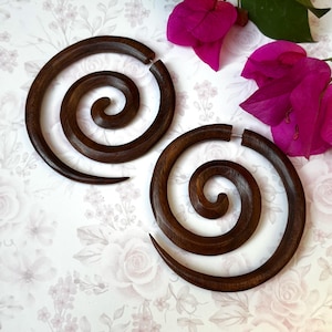 May include: A pair of large, dark brown wooden earrings with a spiral design. The earrings are made of wood and have a natural finish.