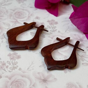 May include: A pair of dark brown wooden earrings with a unique, slightly curved, teardrop-shaped design. The earrings are made of wood and have a natural finish.