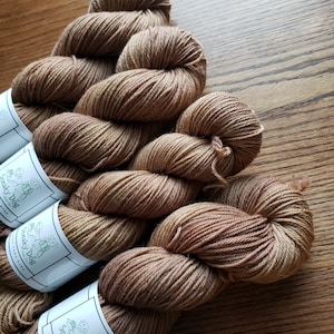 May include: Three skeins of brown hand-dyed yarn with white labels that say "Sneaky Dog Yarn Co. 100g Hand Dyed".