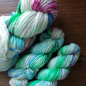 May include: Three skeins of yarn in shades of green, blue, and pink. The yarn is hand-dyed and has a variegated colour pattern.