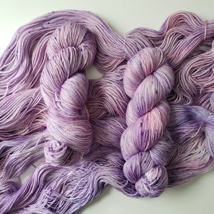 Può includere: Un gomitolo di filato viola e bianco con macchie di colore in tutto. Il filato è morbido e soffice, ed è perfetto per lavorare a maglia o all'uncinetto.