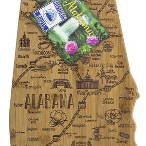 May include: A wooden cutting board shaped like the state of Alabama with cities and towns engraved on the surface. The board is decorated with a small tag that says "Destination Alabama" and a small tag that says "Historic Route".