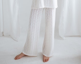 Könnte beinhalten: Weißes Strick-Set mit offenem Gewebe, bestehend aus einem Oberteil mit Kragen und Knöpfen sowie einer Hose mit weitem Bein. Das Outfit hat ein zartes, geometrisches Muster und ist aus leichtem Material gefertigt. Das langärmlige Oberteil und die Hose schaffen einen koordinierten, eleganten Look.