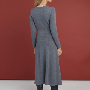 May include: A long-sleeved, mid-length dress in a solid slate gray knit fabric. The garment features a fitted bodice, a defined waistline, and a flared skirt that falls below the knees. The dress is paired with black leather boots.