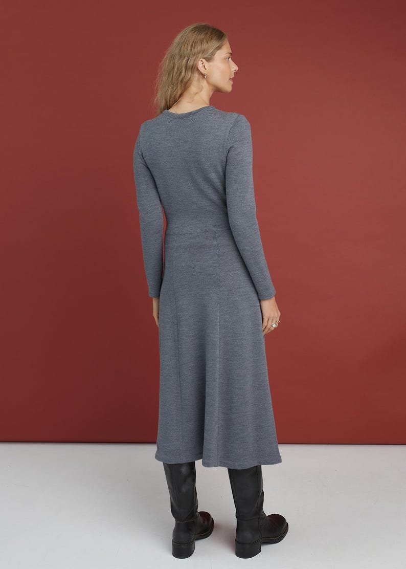 May include: A long-sleeved, mid-length dress in a solid slate gray knit fabric. The garment features a fitted bodice, a defined waistline, and a flared skirt that falls below the knees. The dress is paired with black leather boots.