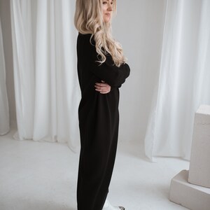 long turtleneck black color knit merino wool dress. blond lady wearing this dress, side look.
