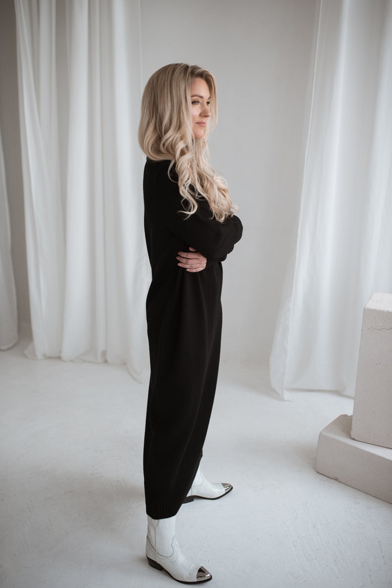 long turtleneck black color knit merino wool dress. blond lady wearing this dress, side look.