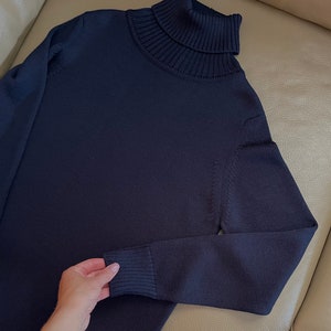 Op de afbeelding: Een donkerblauwe trui met een hoge hals van zacht gebreid materiaal. De trui heeft lange mouwen en een geribbelde kraag.