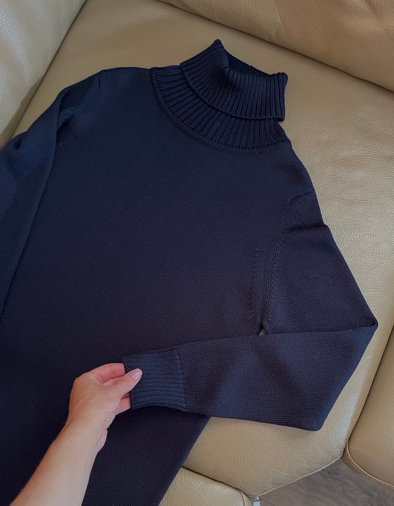 Op de afbeelding: Een donkerblauwe trui met een hoge hals van zacht gebreid materiaal. De trui heeft lange mouwen en een geribbelde kraag.