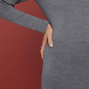 May include: A long-sleeved, charcoal gray knit dress featuring a fine, smooth texture and a fitted bodice that transitions into a slightly flared skirt. The garment is crafted from a soft, uniform material with a subtle ribbed knit pattern throughout.