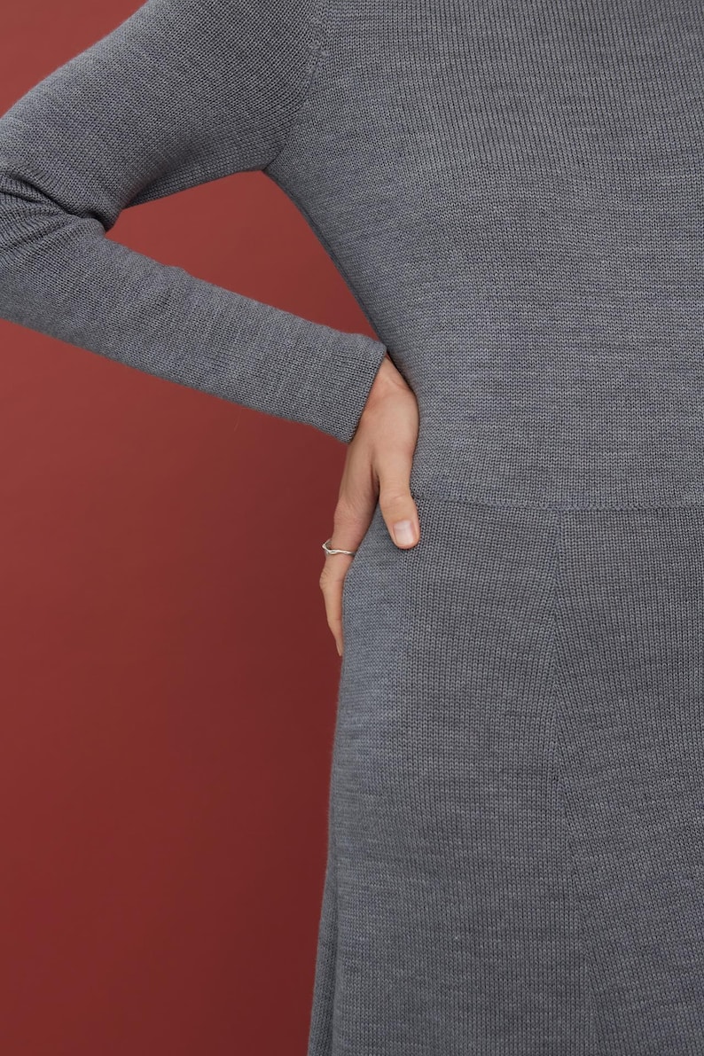 May include: A long-sleeved, charcoal gray knit dress featuring a fine, smooth texture and a fitted bodice that transitions into a slightly flared skirt. The garment is crafted from a soft, uniform material with a subtle ribbed knit pattern throughout.