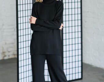 May include: A black long-sleeve turtleneck sweater with a ribbed hem and cuffs, paired with matching black wide-leg knit trousers. The outfit is solid black and features a consistent knit texture throughout the sweater and the pants.