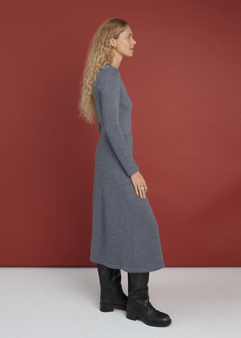 May include: A long-sleeved, mid-length dress in a heathered blue-gray knit fabric. The dress features a fitted bodice, a defined waistline, and a slightly flared skirt that falls below the knee. It is paired with black leather knee-high boots.