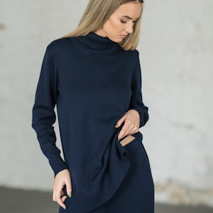 Op de afbeelding: Een donkerblauwe trui met een hoge hals en een bijpassende broek. De trui is lang en heeft een ontspannen pasvorm. De broek is wijd en soepel.