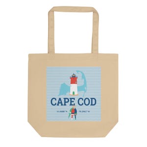 Op de afbeelding: Een beige tote bag met een blauwe en witte illustratie van een vuurtoren en de tekst "CAPE COD" in blauw. De coördinaten "41.6688° N 70.2962° W" zijn onder de tekst afgedrukt.