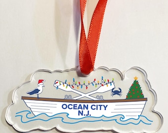 May include: Clear acrylic ornament in the shape of a cloud, featuring a boat with the text "OCEAN CITY N.J." and festive holiday decorations. A red ribbon is attached for hanging.