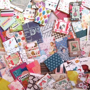 May include: A collection of small, colorful notebooks and journals with various patterns and designs. Some notebooks feature floral prints, while others have text like "Notes" and "Journal." The color palette includes pink, blue, and yellow.