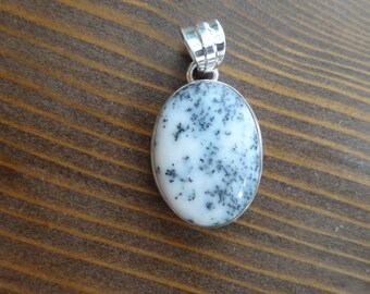 Puede incluir: Un colgante de plata con una piedra de ágata dendrítica blanca y negra. La piedra tiene forma ovalada y un acabado liso y pulido.