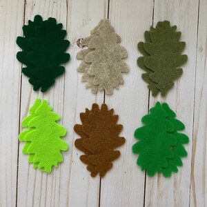 May include: Seven felt leaf shapes in various colors, including green, brown, beige, and lime green. The leaves are layered and have a slightly textured surface.