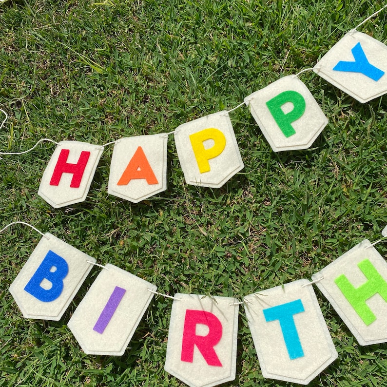 Pu&ograve; includere: Un festoso striscione con la scritta "HAPPY BIRTHDAY" in lettere di feltro colorate. Ogni lettera &egrave; di un colore diverso, attaccata a bandierine bianco sporco. Lo striscione &egrave; infilato su uno spago bianco, perfetto per una festa di compleanno.