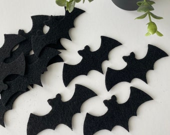 以下が含まれることがあります： 黒いフェルトでカットされたコウモリの切り抜きがいくつかあります。コウモリは白い表面に散らばっています。