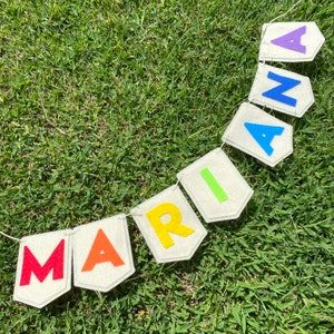 Pu&ograve; includere: Uno striscione fatto a mano che dice "MARIA" con lettere di feltro colorate. Ogni lettera &egrave; di un colore diverso, tra cui rosso, arancione, giallo, verde, blu e viola, attaccata a bandierine bianche sporche. Lo striscione &egrave; infilato su uno spago bianco.