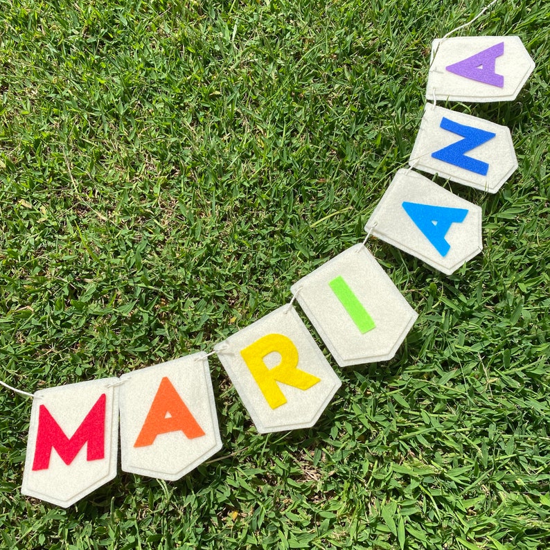 Pu&ograve; includere: Uno striscione fatto a mano che dice "MARIA" con lettere di feltro colorate. Ogni lettera &egrave; di un colore diverso, tra cui rosso, arancione, giallo, verde, blu e viola, attaccata a bandierine bianche sporche. Lo striscione &egrave; infilato su uno spago bianco.