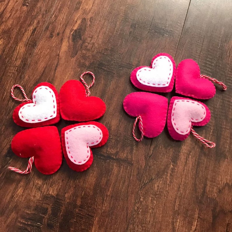 Op de afbeelding: Vier vilt harten in rood, roze en wit, met witte stiksels rond de randen. Elk hart heeft een touwtje om op te hangen.