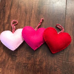 Op de afbeelding: Drie vilten harten in roze, rood en felroze, elk met een wit en rood touwtje.
