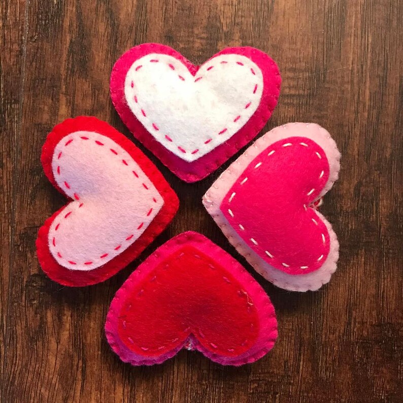 Op de afbeelding: Vier vilten harten in verschillende tinten roze en rood, gerangschikt in een cirkel op een houten oppervlak.