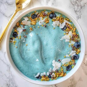 Op de afbeelding: Een blauwe smoothiebowl bedekt met granola, kokosvlokken en blauwe bessen.