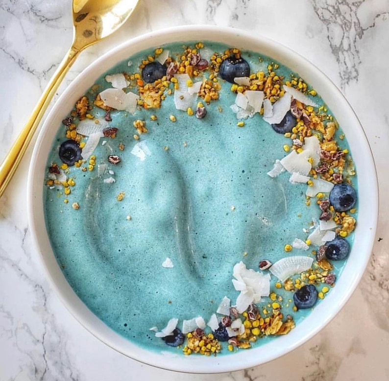 Op de afbeelding: Een blauwe smoothiebowl bedekt met granola, kokosvlokken en blauwe bessen.