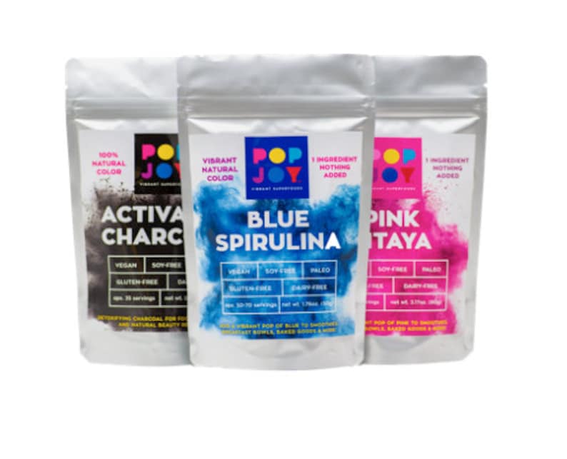 Op de afbeelding: Drie zakjes met natuurlijk voedselkleurpoeder. De zakjes zijn gelabeld met "Activa Charcoal", "Blue Spirulina" en "Pink Pitaya". Elk zakje heeft een afbeelding van een levendige kleurwolk en vermeldt de ingredi&euml;nten als "1 ingredi&euml;nt, niets toegevoegd".