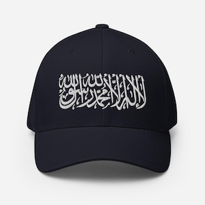 May include: A navy blue baseball cap featuring white embroidered Arabic script across the front. The cap has a curved peak and a structured design. The text is a key design element.