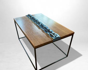May include: A modern coffee table with a rectangular wooden top and a black metal frame. The table features a central, textured, blue-gray decorative element. The wooden top is approximately 40 inches long and 20 inches wide.