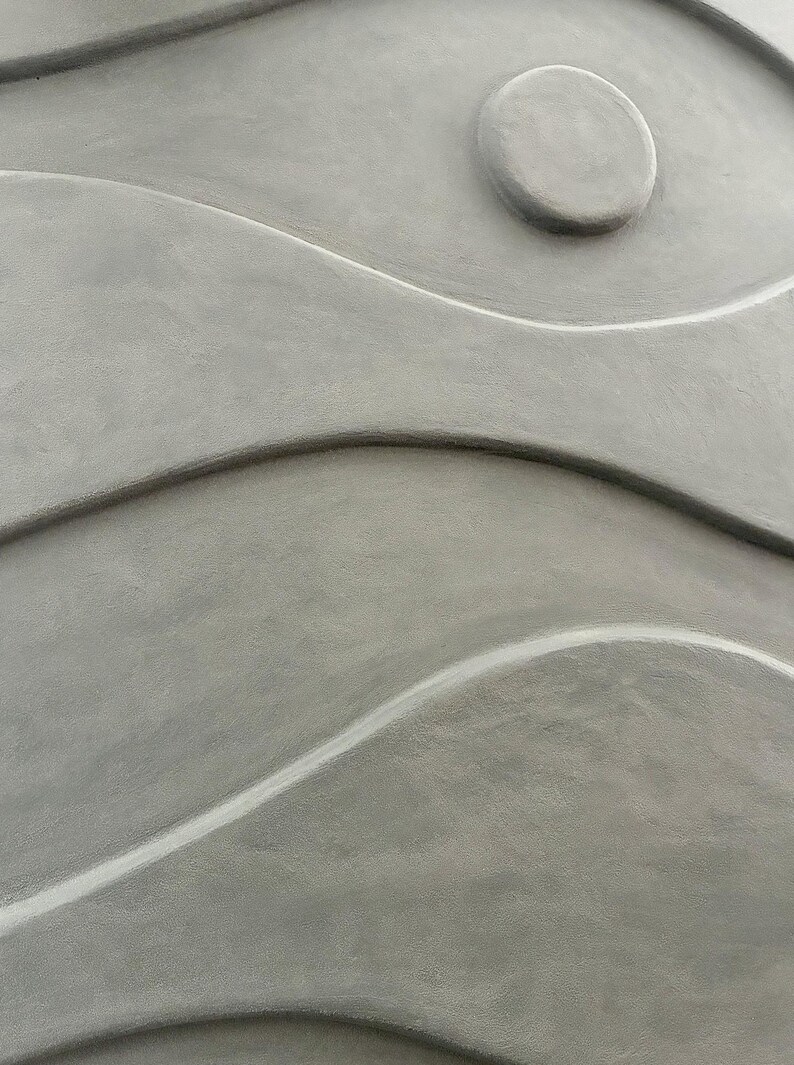 May include: Abstract gray wall art with a textured surface. The design features flowing, wave-like shapes and a circular element, creating a sense of movement and depth. The artwork is a neutral color, suitable for various interior styles.