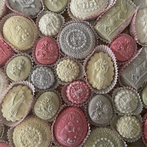 May include: A collection of white, pink, and gray cookies with various embossed designs, including bunnies, flowers, and geometric patterns. The cookies are arranged in a circular pattern on a white surface.