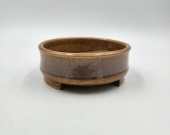 Op de afbeelding: Een bruine keramische bonsai pot met een ronde vorm en drie kleine voetjes. De pot heeft een gespikkelde glazuur.