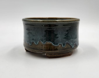 Op de afbeelding: Een kleine, ronde, groene en bruine keramische bonsai pot met vier voetjes.