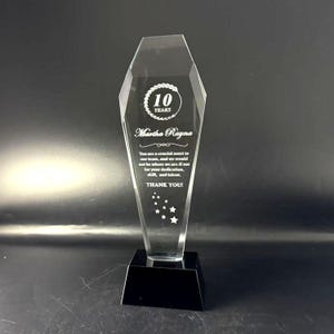 Op de afbeelding: Een heldere, gefacetteerde acryl award trofee met een zwarte voet. De trofee is voorzien van een ge&euml;tst ontwerp met de tekst 10 YEARS, de naam Martha Rayna, een dankbetuiging en een groepje kleine sterren onderaan het heldere oppervlak.