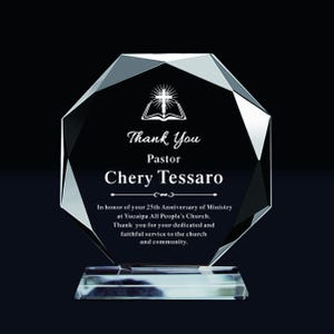 Può includere: Un premio in vetro trasparente e sfaccettato con base rettangolare. Il premio presenta il testo "Thank You Pastor Chery Tessaro" e una dedica per 25 anni di ministero presso la Yucaipa All People's Church. Una croce e un libro aperto in alto.