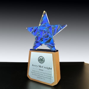 May include: A blue crystal star award on a wooden base with a silver plaque that reads "Jerry McCreight" and a message of thanks for hard work and dedication. The plaque also features a small image of the United States seal.