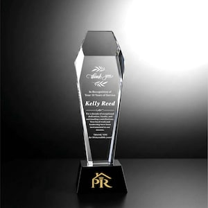 May include: A clear, faceted crystal award trophy featuring the text "thank you" with leaf accents, "In Recognition of Your 10 Years of Service", "Kelly Reed", and a paragraph of appreciation. The base is black with a gold "PR" logo and crown icon.